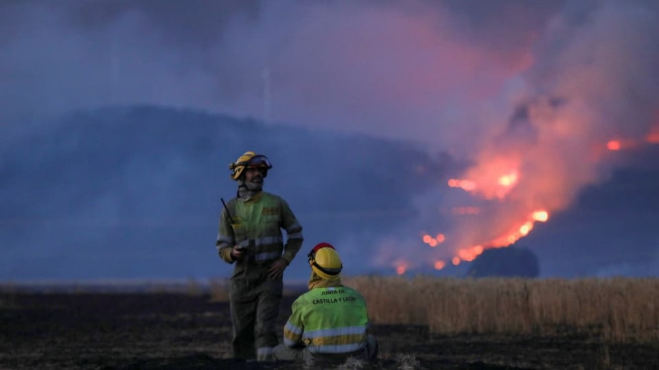 Two firefighters in front of a forest fire in Spain.