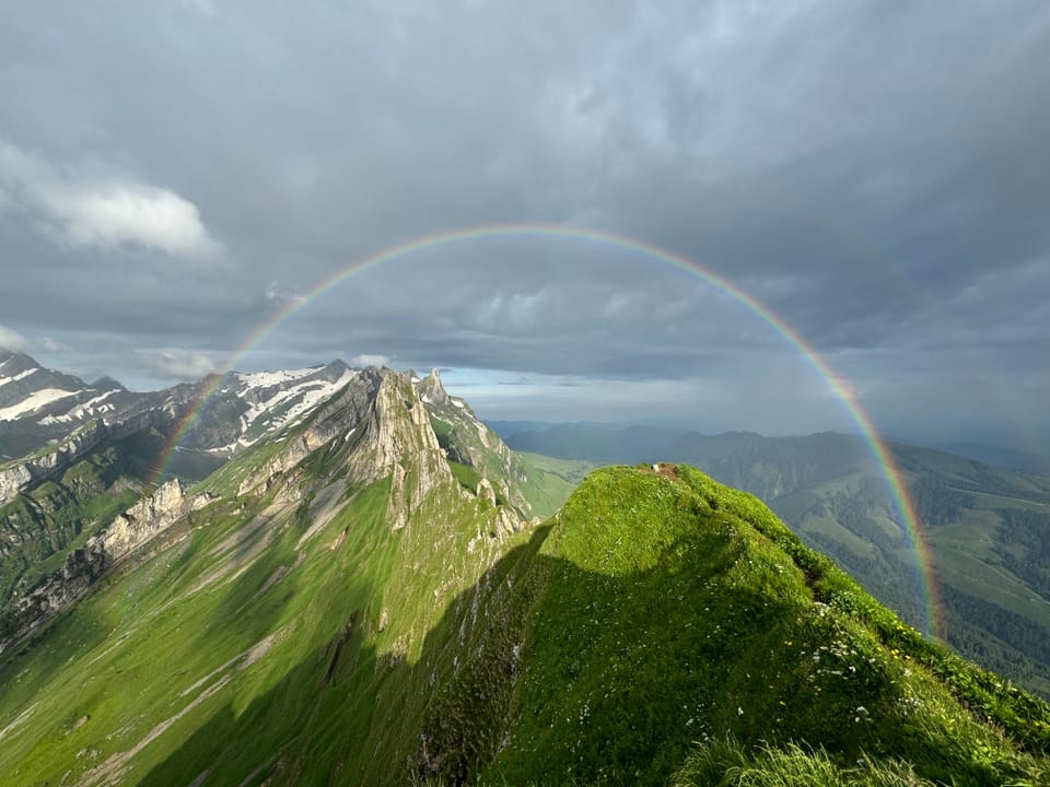 Ein doppelter Regenbogen über steilen, grünen Bergen