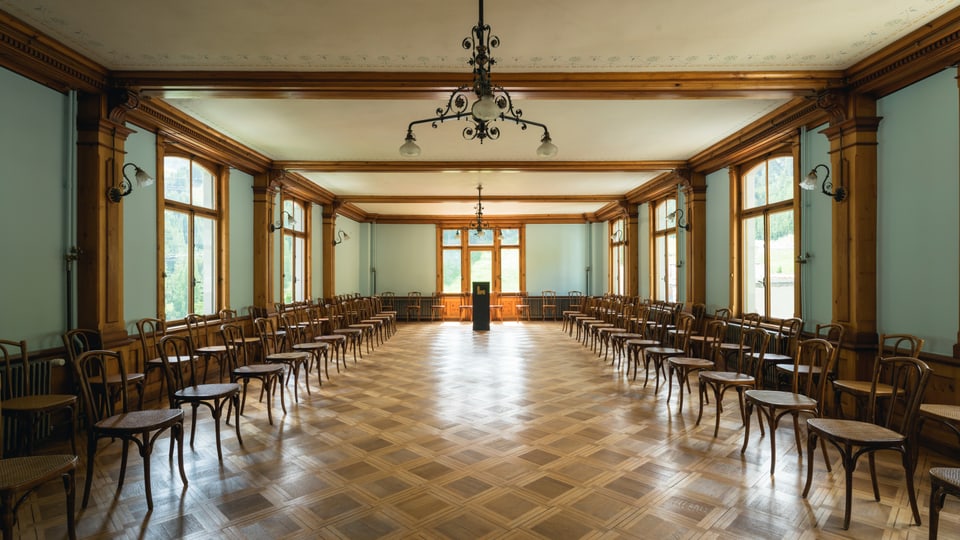 Grosser Saal mit Parkettboden und Stühlen links und rechts.