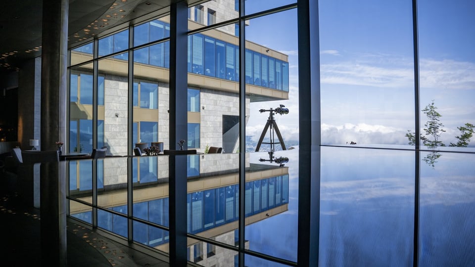Reflexion eines Gebäudes und Himmels in einer Glaswand und Wasserfläche.
