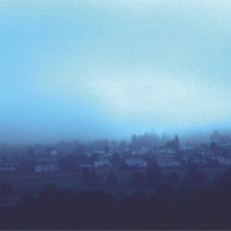 Eine Wolke hängt tief über einem Dorf, das Sonnenlicht kann man nur noch schwach erkennen.