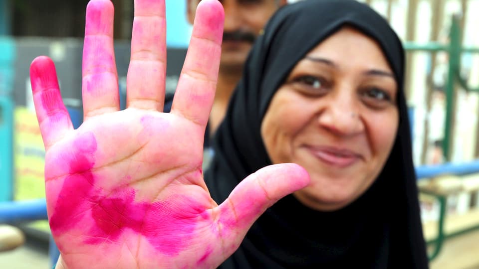 Eine ägyptische Hausfrau streckt ihre Handfläche in die Kamera und lacht. Die Hand ist rot von der Wahltinte.