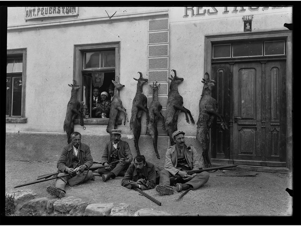 Fotografia en alv e nair da 4 chatschader e lur chamutschs davant ustaria a Scuol