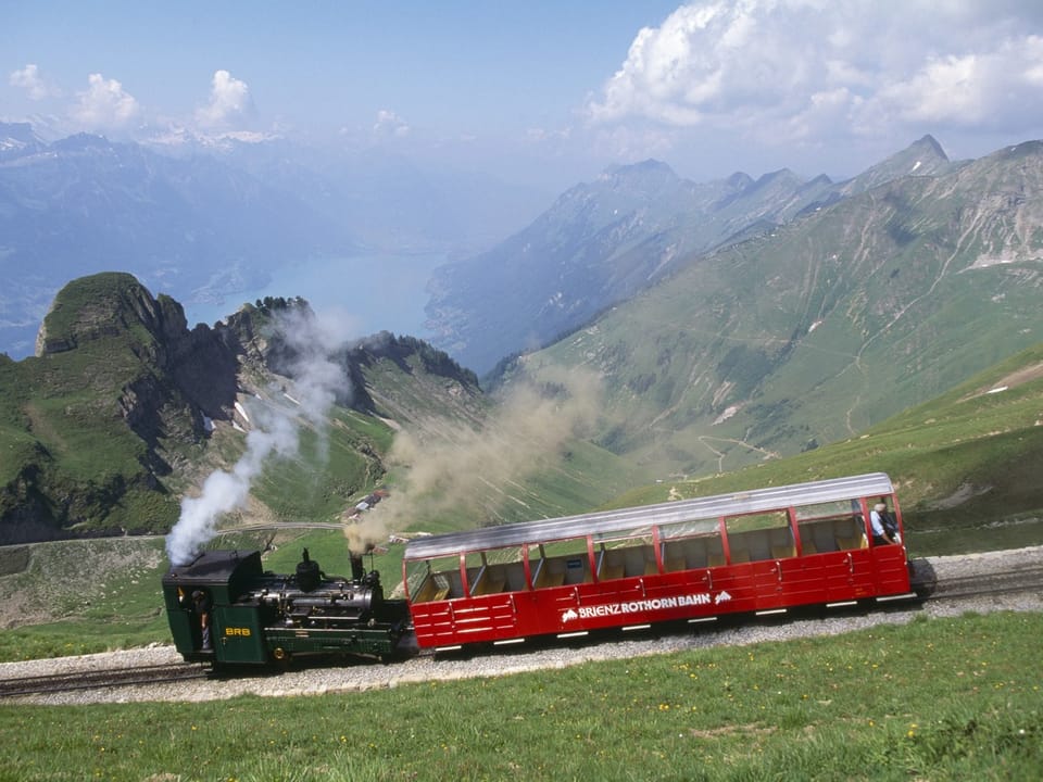 Eine Dampflokomotive mit einem roten Aussichtswagen im Gebirge. 