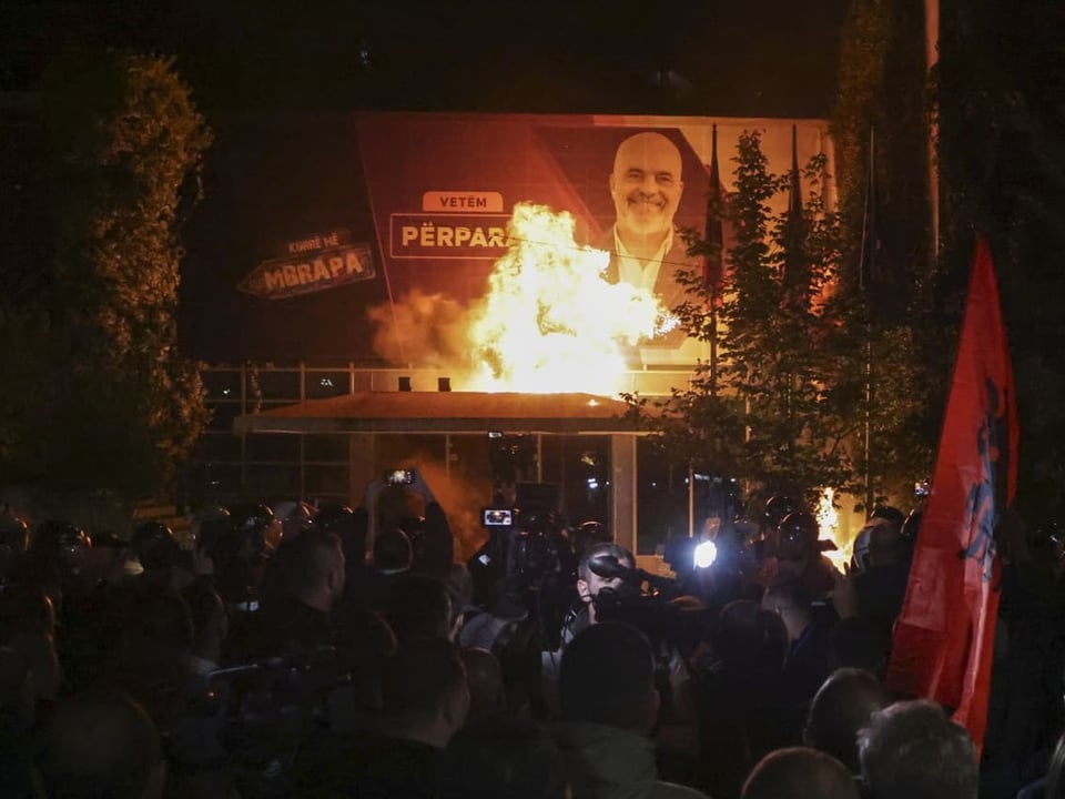 Nachtprotest mit Feuer vor beleuchtetem Gebäude.