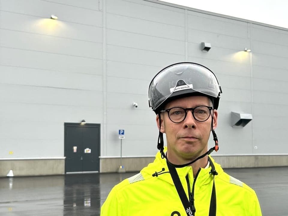 Person in gelber Jacke und Helm vor grauer Gebäudewand.