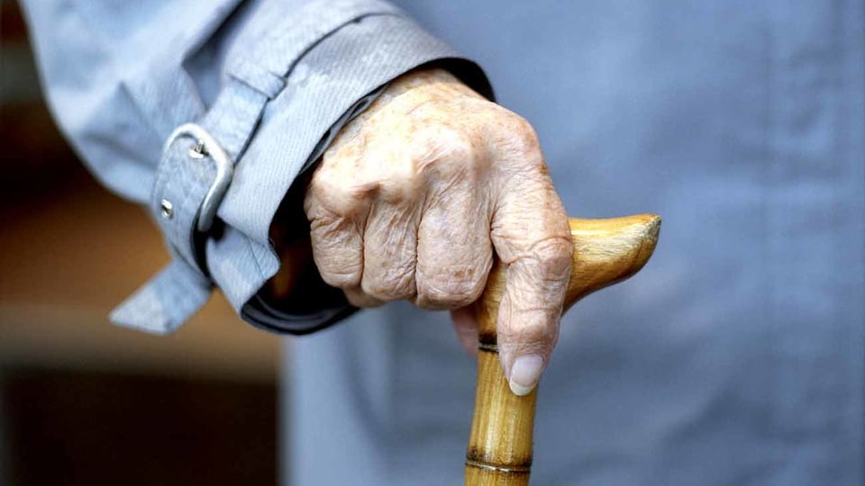 Eine alte Frau hält einen Stock in der Hand.