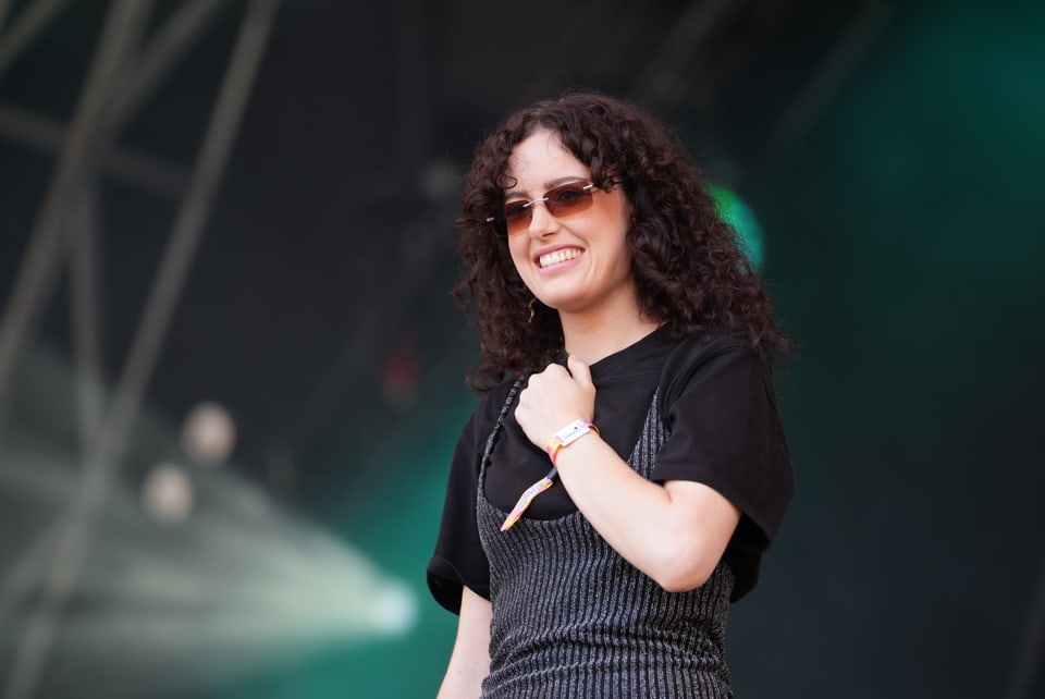 Frau mit lockigem Haar und Sonnenbrille auf der Bühne am Open Air Lumnezia 2024.