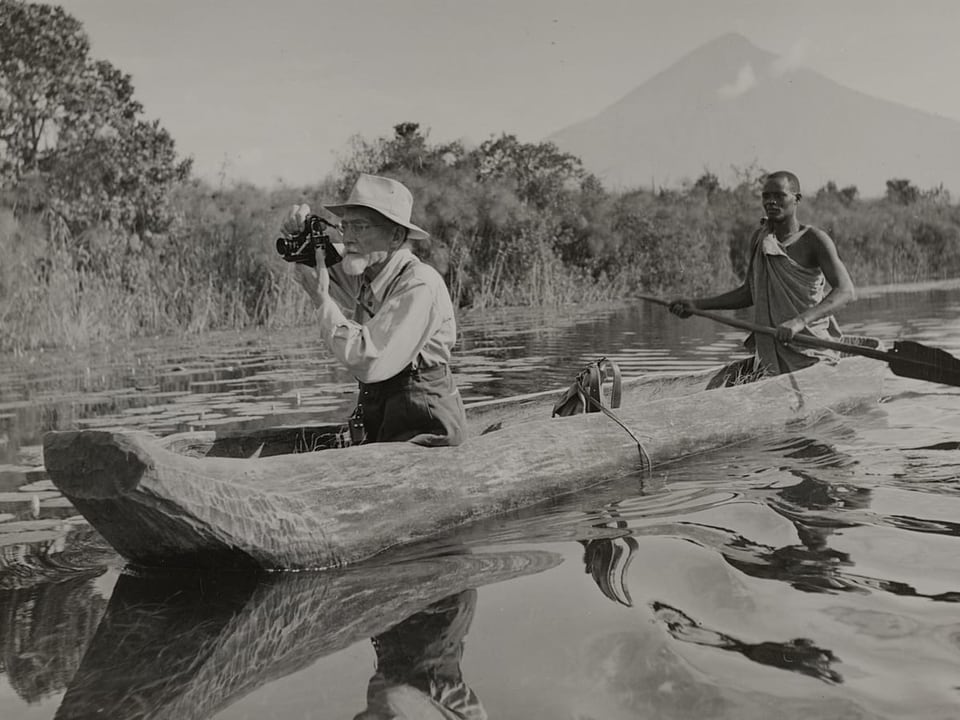 Mann mit Kamera und Führer in Kanue auf Fluss mit Vulkan im Hintergrund.