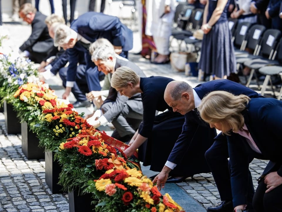 Menschen legen Blumen bei einer Gedenkveranstaltung nieder.