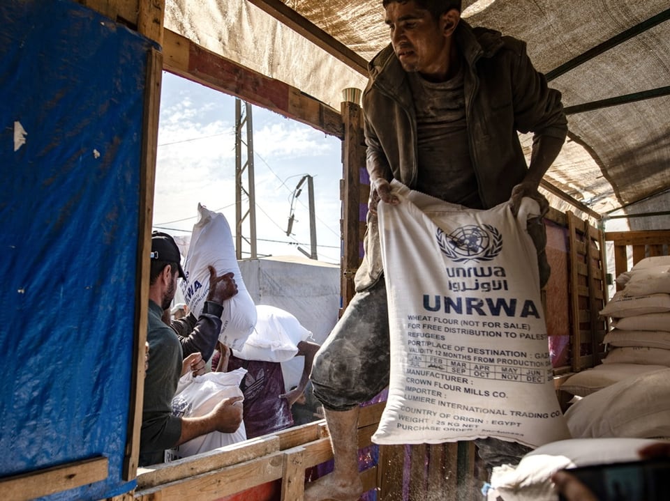 Männer entladen UNRWA-Säcke aus einem Lastwagen.