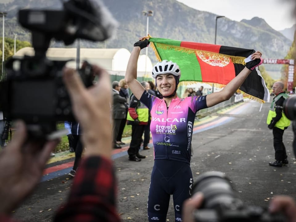 Radrennfahrerin jubelt mit Flagge, Fotografen im Vordergrund.