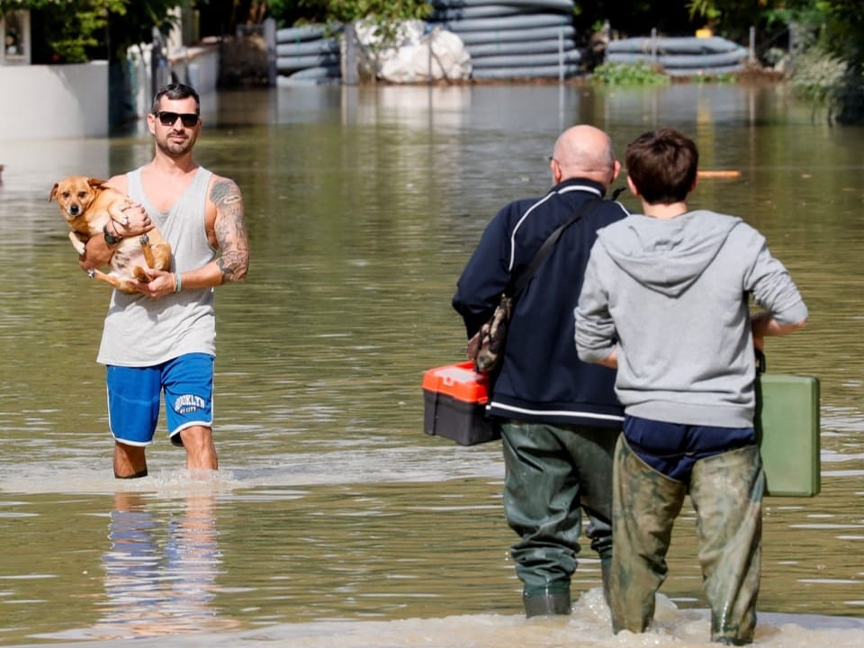 Menschen waten durch Hochwasser mit einem Hund.