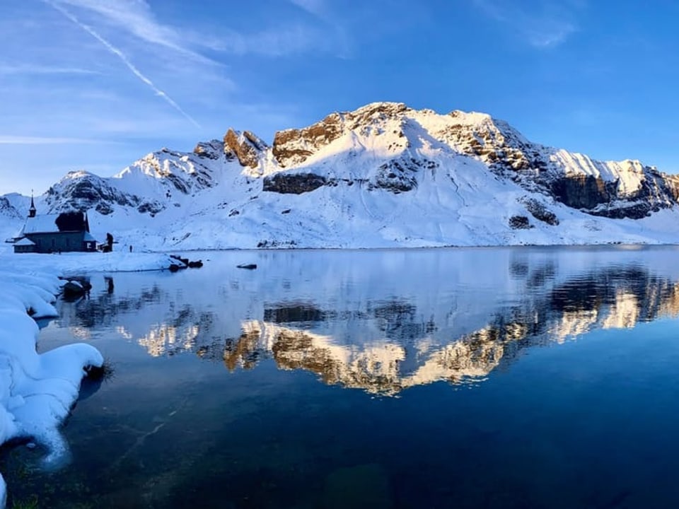 Schneebedeckte Berge spiegeln sich in einem ruhigen See.