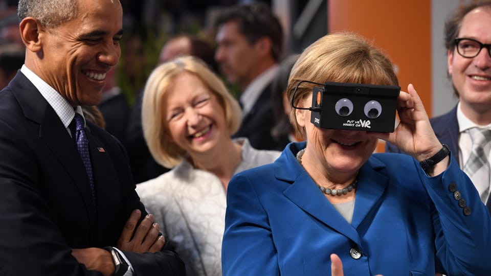 Angela Merkel hält sich ein Spielzeug mit zwei Augen vors Gesicht