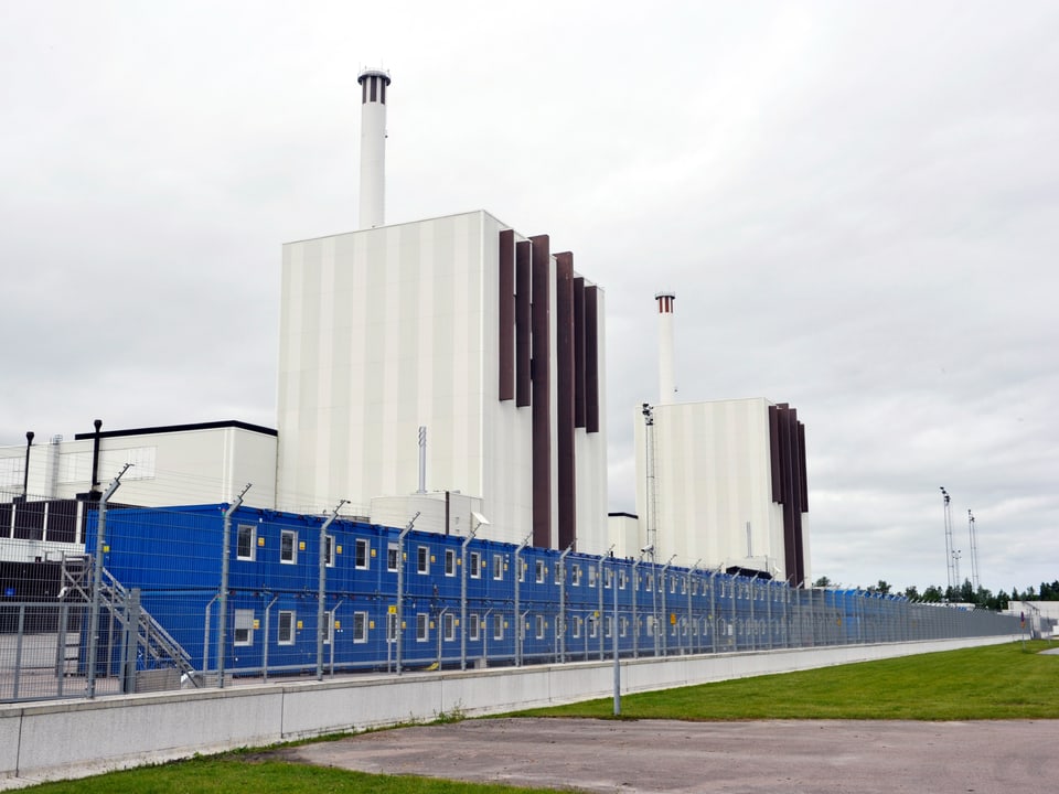 Zwei hohe, weisse Industriegebäude hinter einem Zaun.