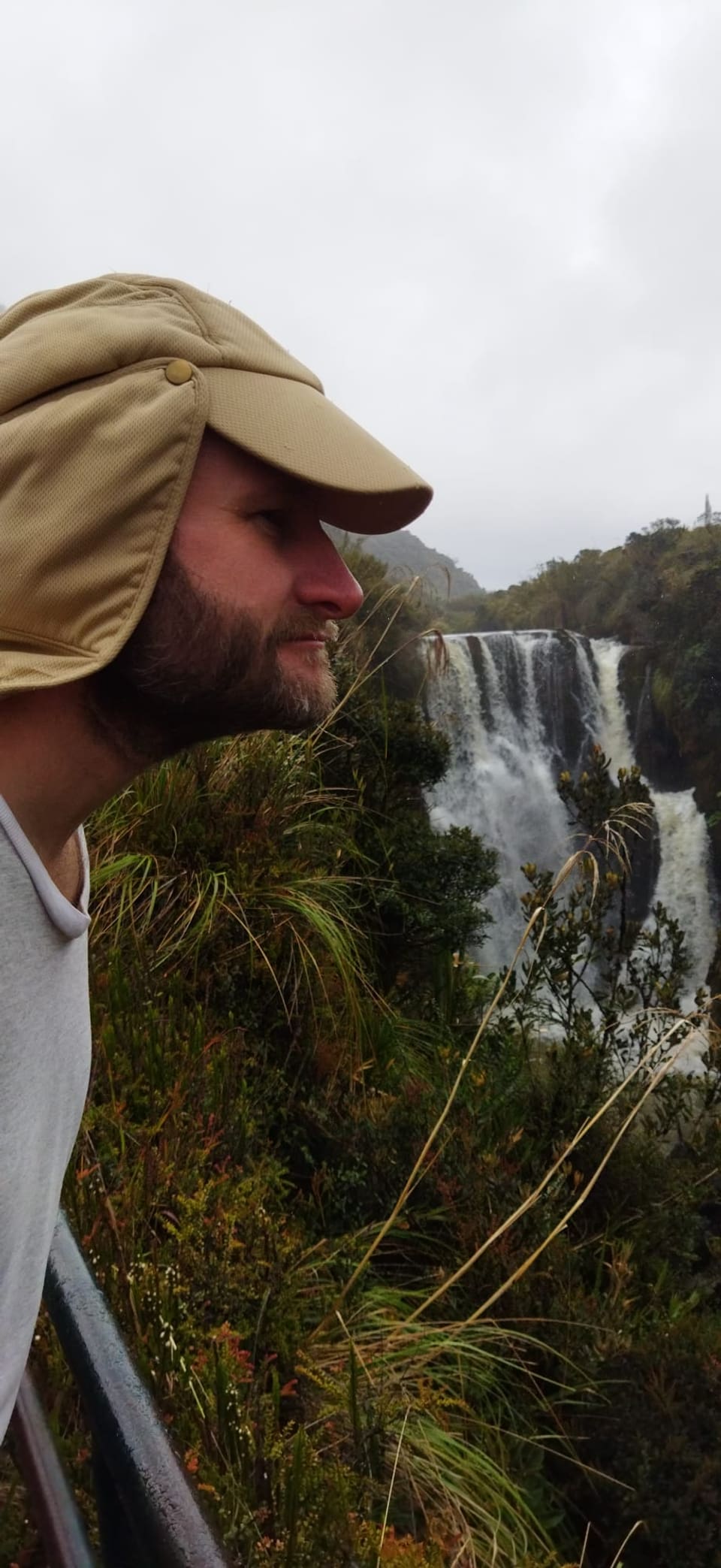 Person mit Mütze steht vor einem Wasserfall.