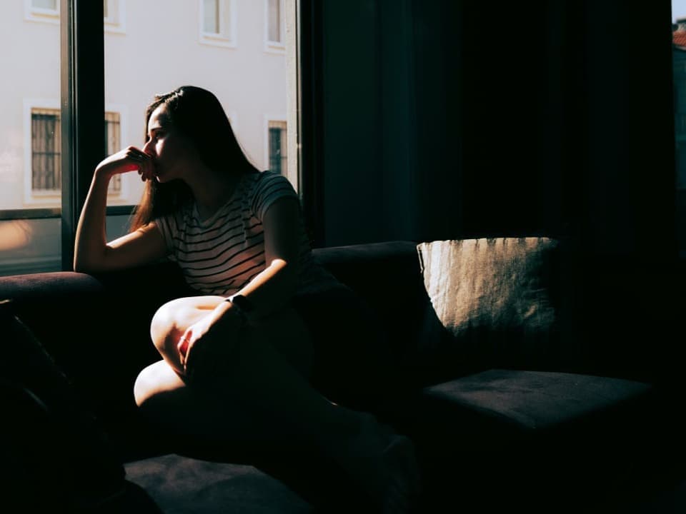 Eine Frau sitzt auf dem Sofa und blickt in die Ferne.