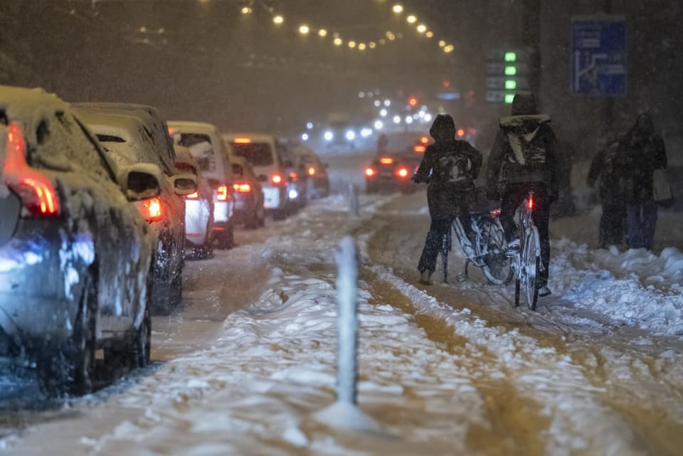 Schneeverkehr mit Autos und Radfahrern bei Nacht.