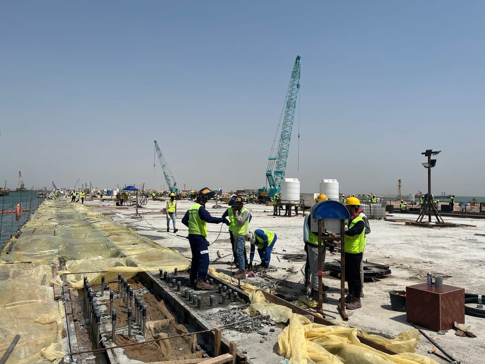 Arbeiter auf einer Baustelle bei sonnigem Wetter mit Kränen im Hintergrund.