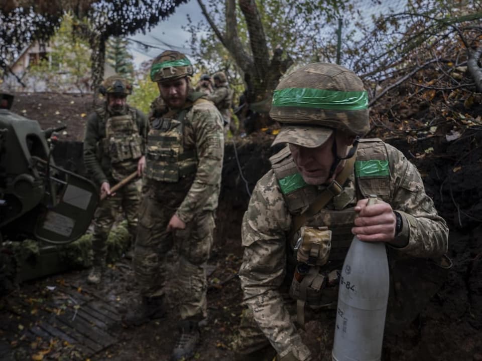 Soldaten in Tarnkleidung mit Artilleriegerät im Wald.