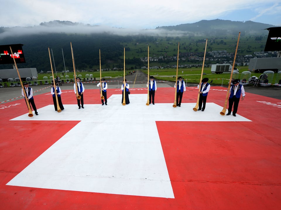 Alphornbläse auf dem Rollfeld, auf dem die Schweizer-Flagge zu sehen ist.