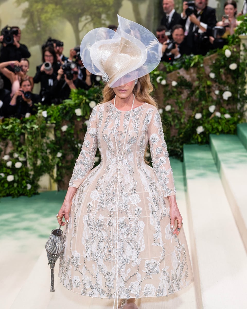 Frau in weissem Glitzerkleid mit voluminösem Kopfschmuck.