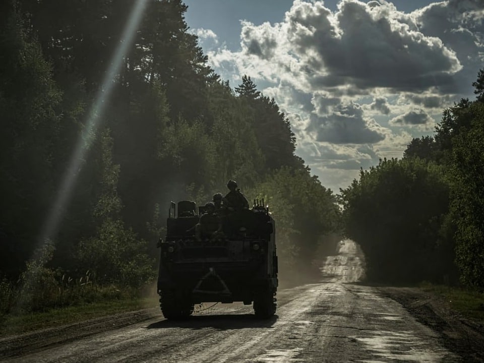 Militärfahrzeug auf einer staubigen Strasse im Wald bei Sonnenuntergang.