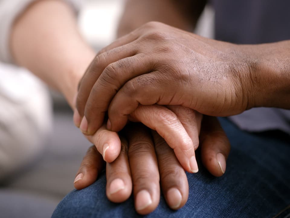 Nahaufnahme einer Hand, die die Hand einer anderen Person auf dem Knie hält.