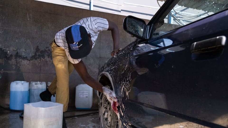 Mann wäscht Rad eines schwarzen Autos.