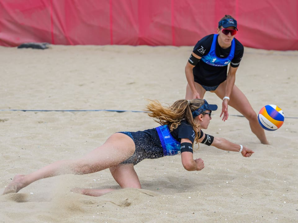 Zwei Frauen spielen Beachvolleyball, eine taucht nach dem Ball.