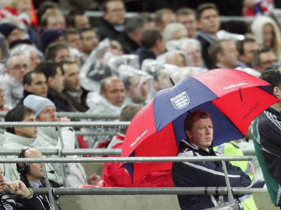 Fussballtrainer unter Regenschirm im Stadion.