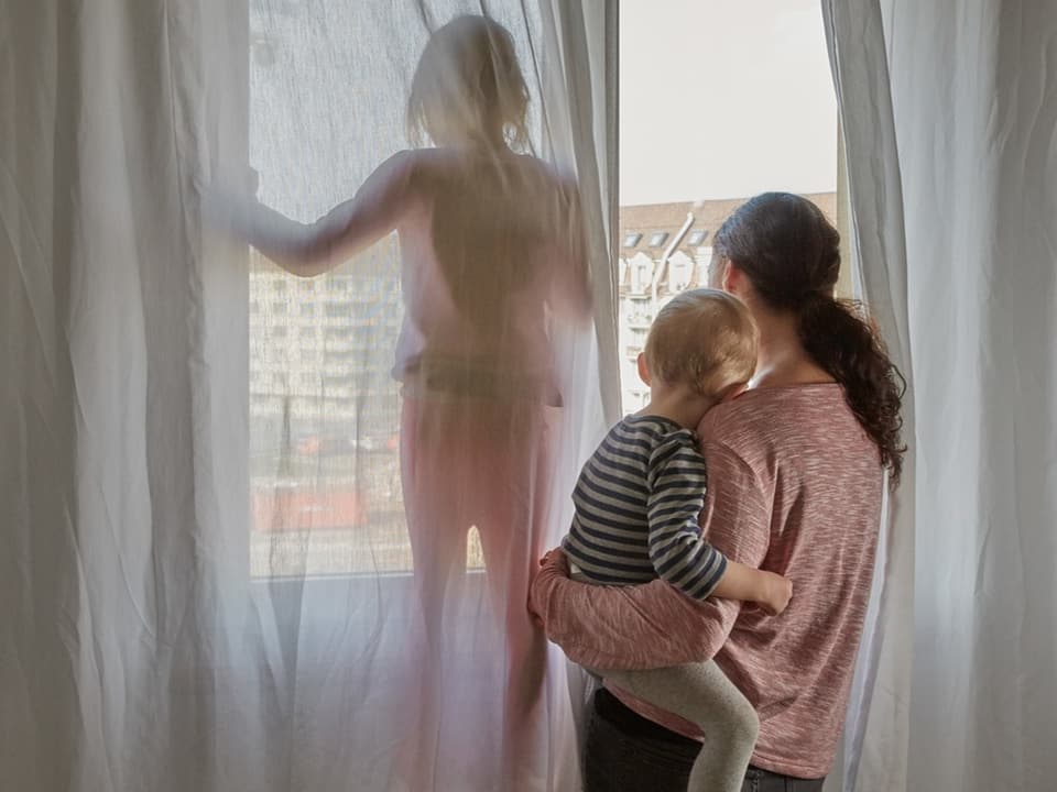 Frau mit Kleinkind und Kind am Fenster mit Vorhängen.