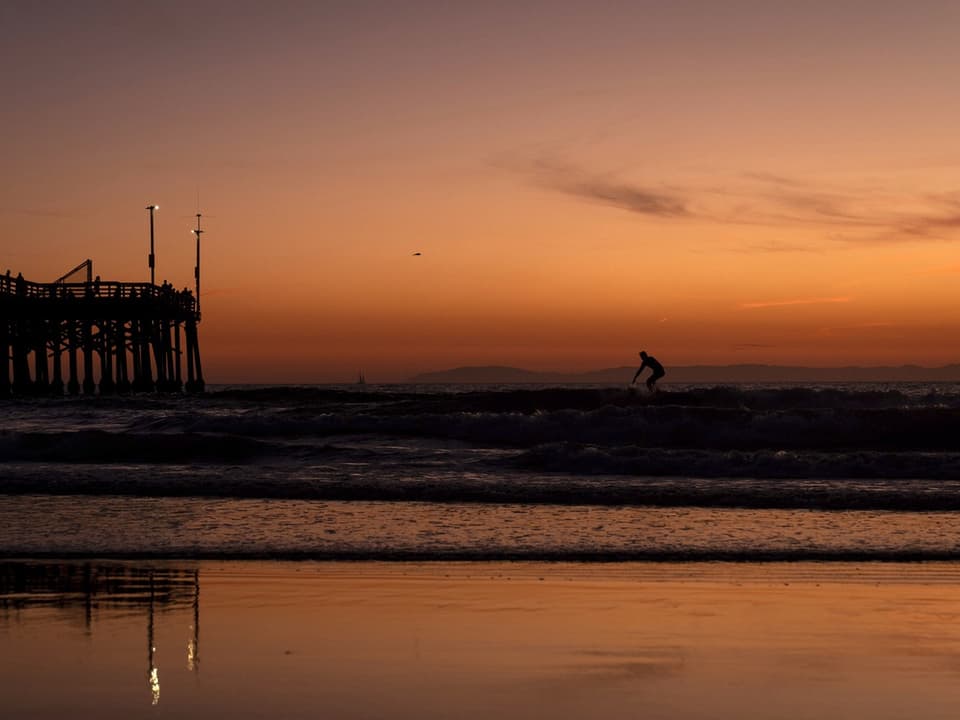 Surfer bei Sonnenuntergang am Pier.