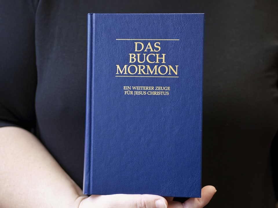 Person hält das Buch 'Das Buch Mormon'.