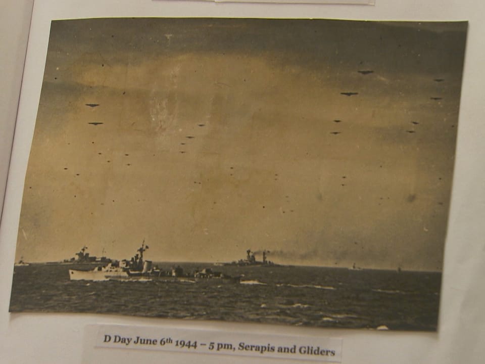 verblichenes schwarzweiss-foto vom Meer mit einer Kriegsschiff darauf und Flugzeugen als Punkte am Horizont