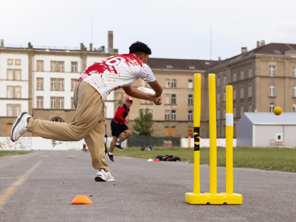 Junge Männer beim Cricketspiel auf einer Strasse vor Gebäuden.