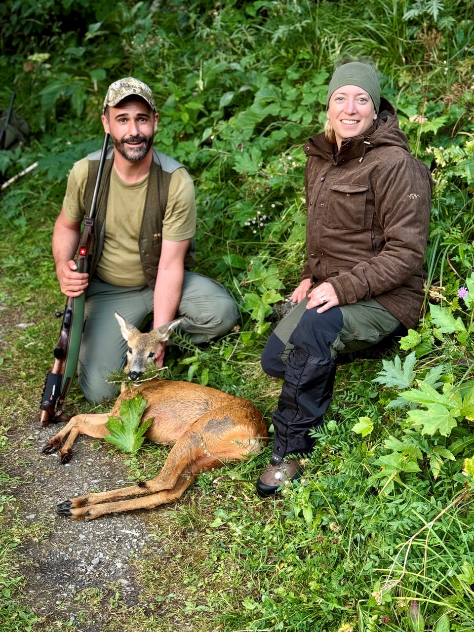 Zwei Jäger posieren neben einem Reh im Wald.