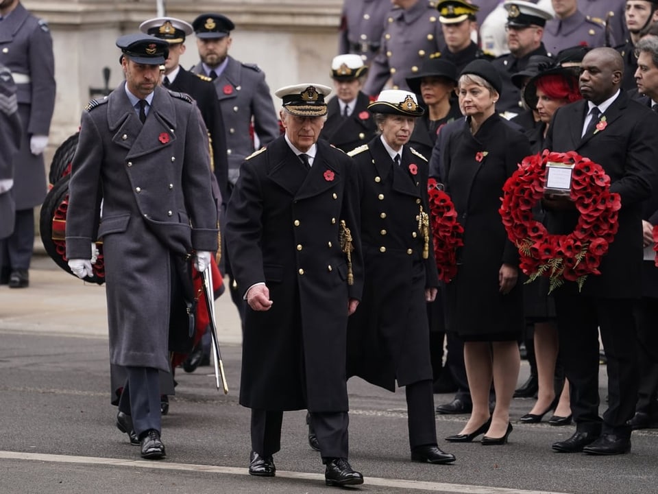 Menschen in Militäruniformen und formeller Kleidung bei einer Gedenkveranstaltung.