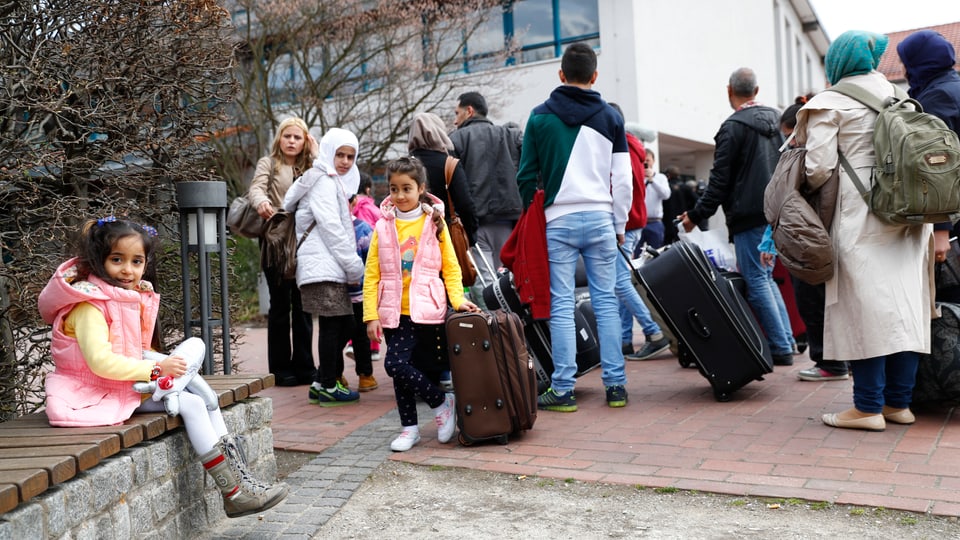 Migranten mit Koffern vor einem grossen Gebäude in Deutschland.