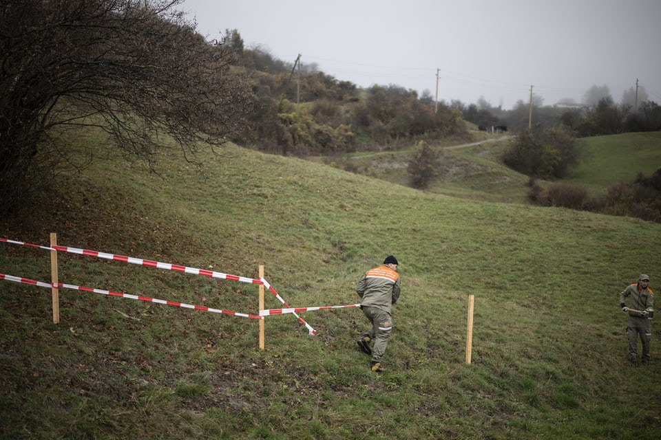 Arbeiter mit Absperrband auf grüner Wiese.