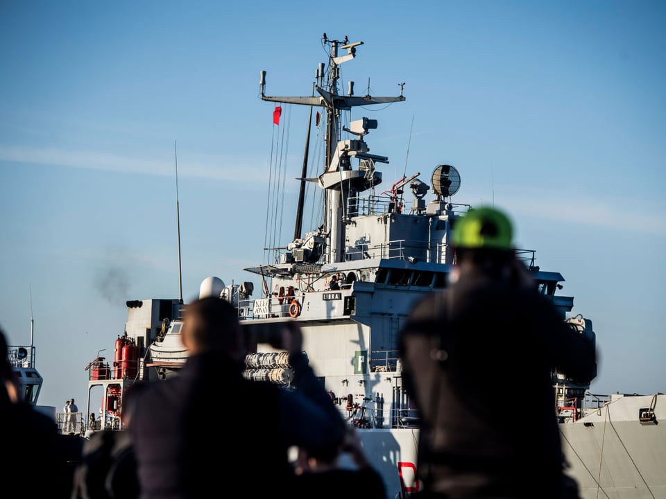 Menschen fotografieren ein Marineschiff im Hafen.