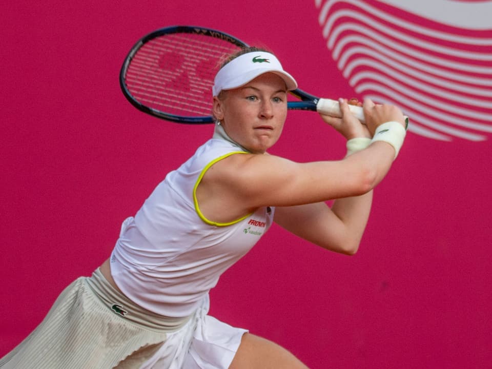 Tennisspielerin in weissem Outfit beim Rückschlag auf pinkem Hintergrund.