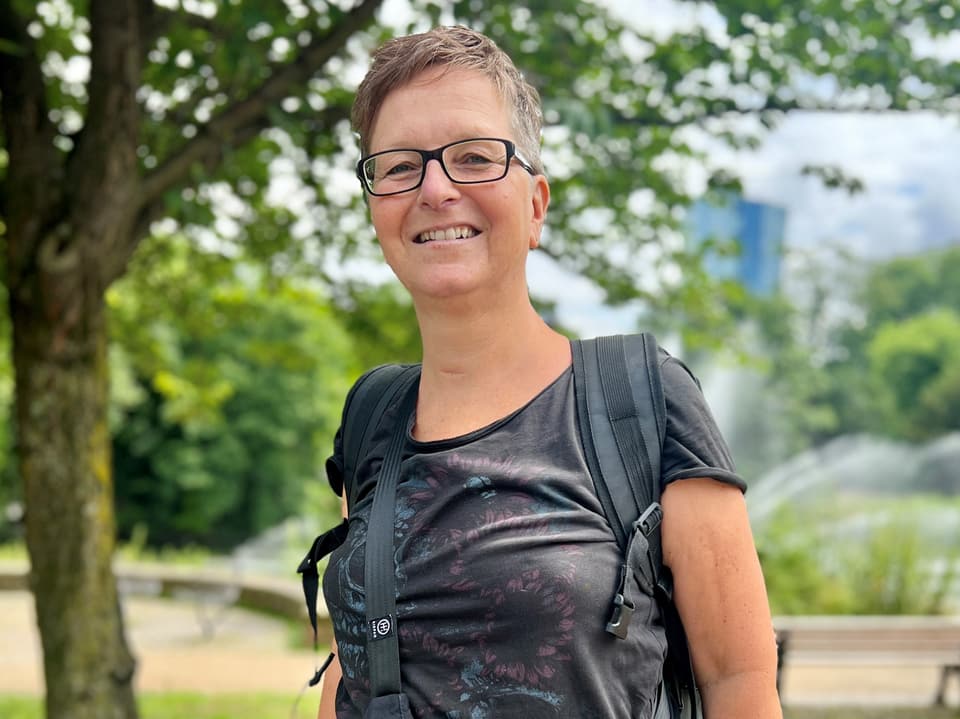 Frau mit Brille und Rucksack lächelt im Park.