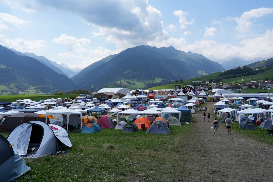 Zeltlager auf einer Wiese mit Bergen im Hintergrund am Open Air Lumnezia 2024.