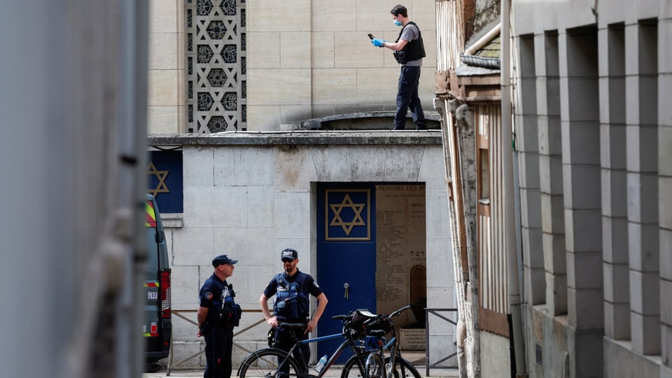 Polizisten vor Gebäude mit Davidstern, Mann auf Dach.