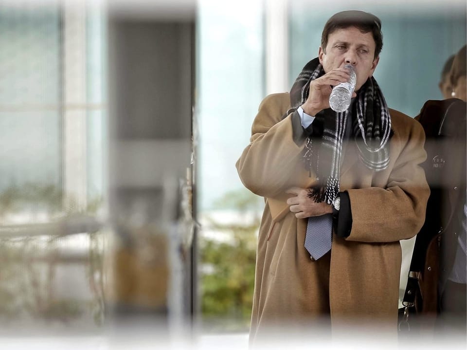 Mann im Mantel trinkt aus einer Wasserflasche.