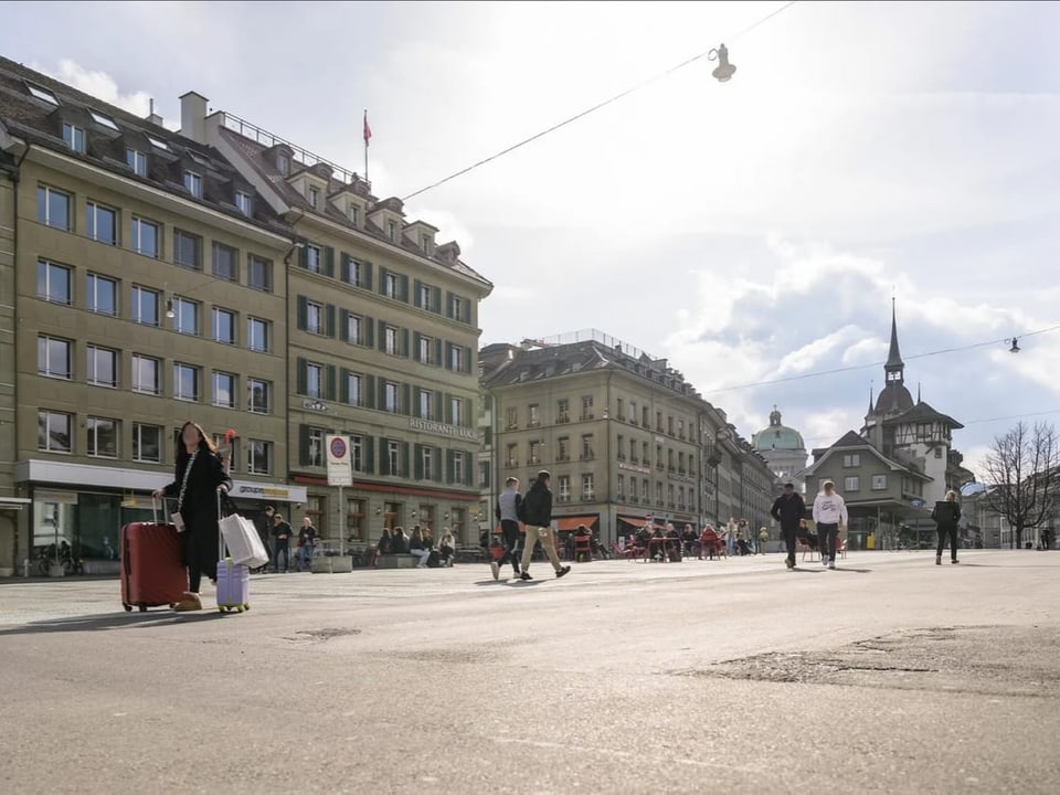 Menschen auf einem Platz in einer Stadt mit alten Gebäuden und Kirchturm.