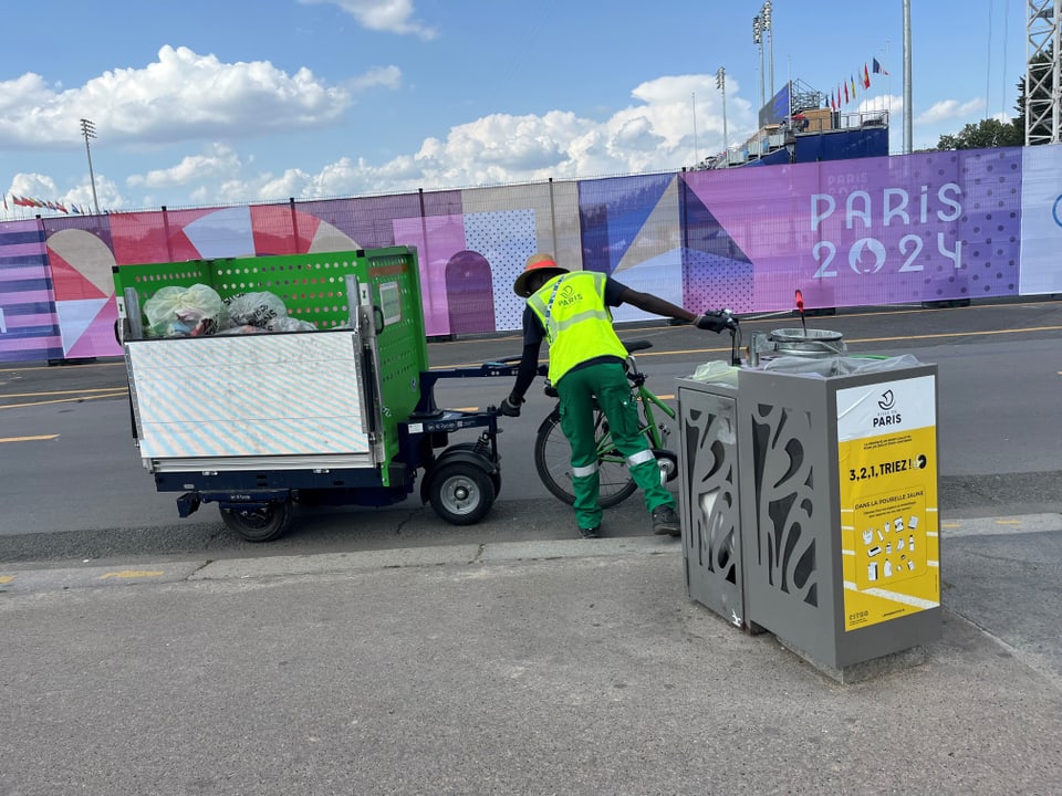 Arbeiter in gelber Weste mit Reinigungsfahrzeug vor PARIS 2024 Wand.