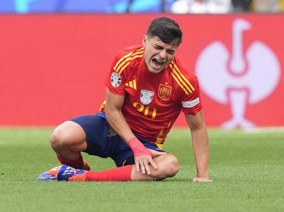 Fussballspieler in spanischem Trikot kniet auf Rasen und schreit vor Schmerzen.
